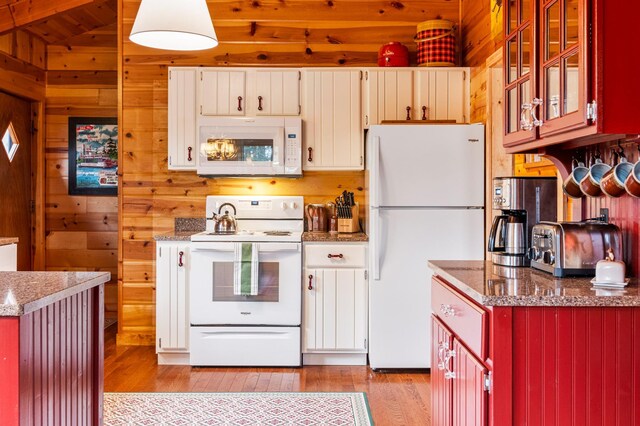 kitchen featuring white appliances, light wood finished floors, wooden walls, vaulted ceiling, and glass insert cabinets