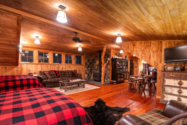 living area featuring wood walls, wooden ceiling, a wood stove, and hardwood / wood-style flooring