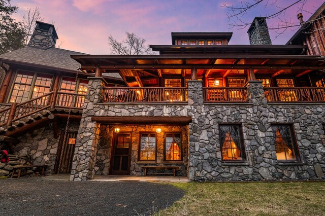 back of property with a balcony, a chimney, stone siding, and a yard