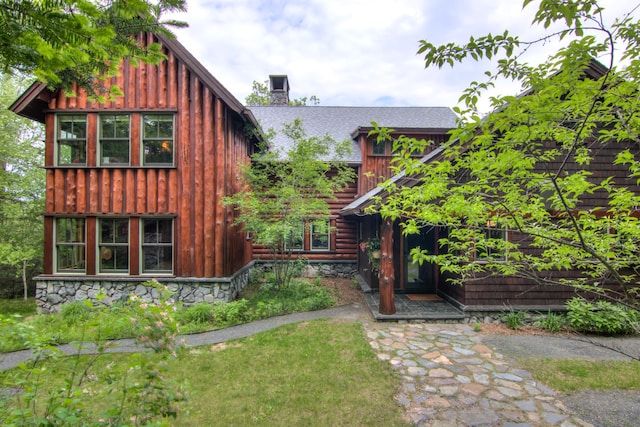 view of front of property with a chimney, board and batten siding, stone siding, and a shingled roof