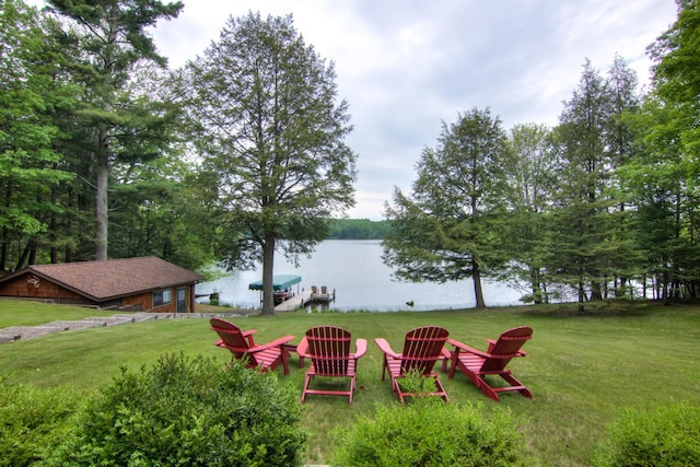 view of grassy yard featuring a water view, a fire pit, and a dock