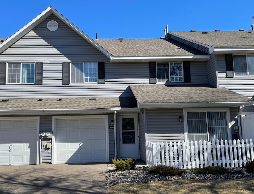 multi unit property with driveway, a shingled roof, an attached garage, and fence