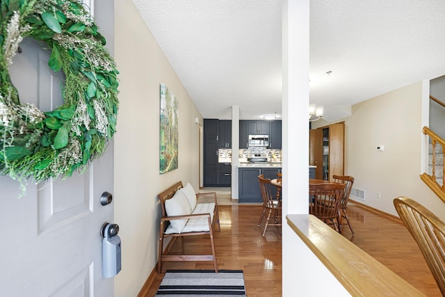 foyer with stairway, baseboards, visible vents, light wood finished floors, and a textured ceiling