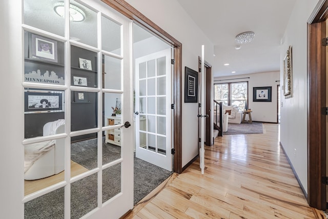 hallway featuring french doors, baseboards, and light wood finished floors