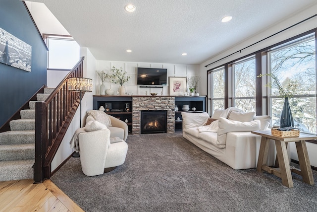 living area featuring a textured ceiling, a stone fireplace, recessed lighting, wood finished floors, and stairway