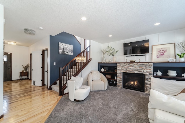 living room featuring a textured ceiling, stairs, wood finished floors, and a stone fireplace