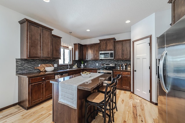 kitchen with dark brown cabinetry, stainless steel appliances, a breakfast bar, a sink, and light wood-type flooring