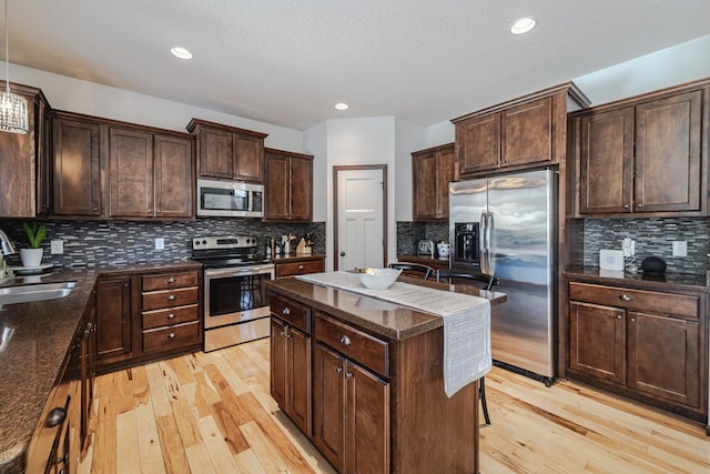 kitchen with stainless steel appliances, light wood finished floors, a sink, and a center island