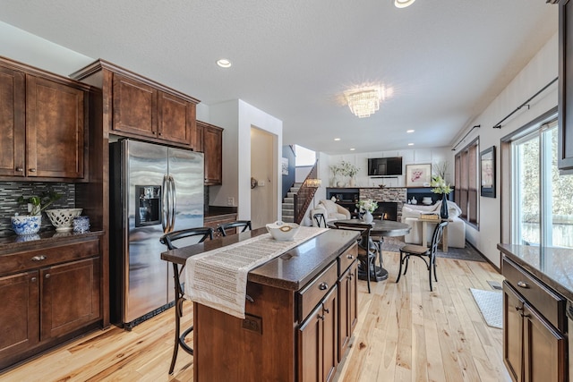 kitchen featuring a fireplace, a kitchen breakfast bar, light wood-type flooring, backsplash, and stainless steel fridge with ice dispenser