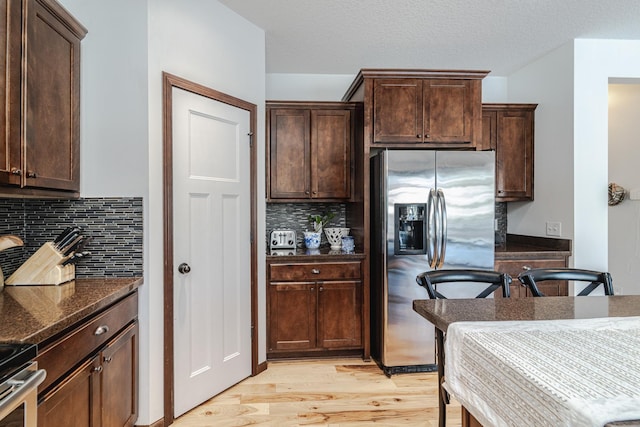 kitchen with dark brown cabinetry, light wood-style flooring, appliances with stainless steel finishes, and dark stone counters