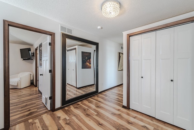 hall with light wood-type flooring, visible vents, and a textured ceiling