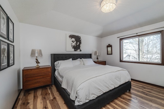 bedroom with vaulted ceiling, wood finished floors, and baseboards