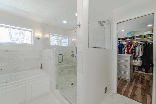 full bathroom with wood finished floors, visible vents, a spacious closet, a bath, and a stall shower