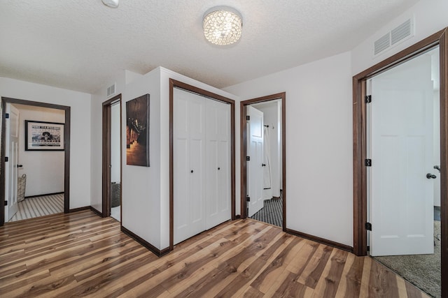 unfurnished bedroom with a textured ceiling, a closet, wood finished floors, and visible vents