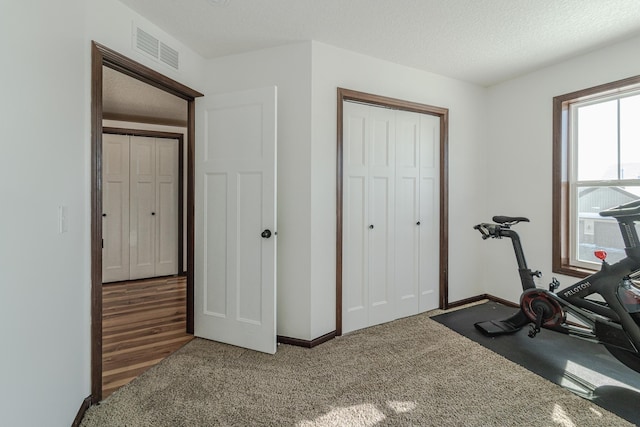 workout area with a textured ceiling, carpet floors, visible vents, and baseboards