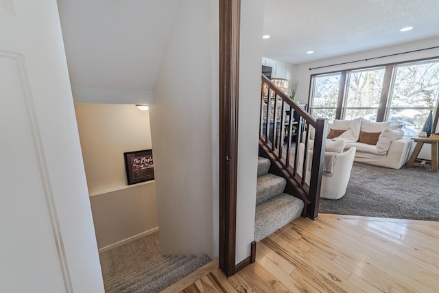 stairway featuring recessed lighting, a textured ceiling, baseboards, and wood finished floors