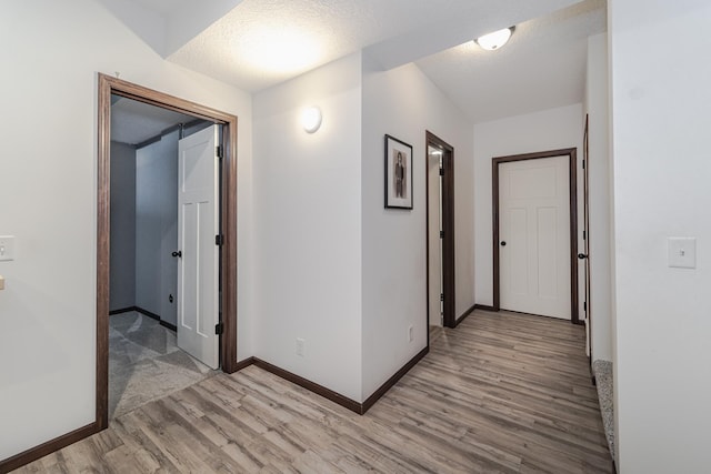 hall with a textured ceiling, baseboards, and light wood-style floors