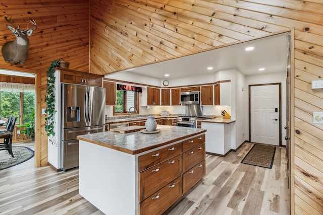 kitchen with light wood-type flooring, wooden walls, appliances with stainless steel finishes, and a center island