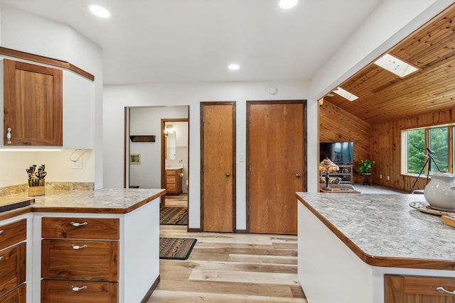 kitchen with recessed lighting, light countertops, light wood-style floors, brown cabinetry, and lofted ceiling with skylight