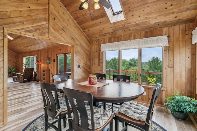 dining area with a healthy amount of sunlight, a skylight, light wood-type flooring, and wooden walls