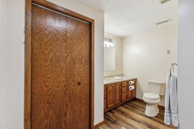 bathroom with visible vents, toilet, wood finished floors, a textured ceiling, and vanity