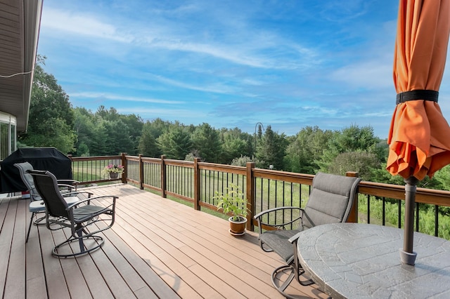 wooden terrace featuring outdoor dining space, a view of trees, and grilling area