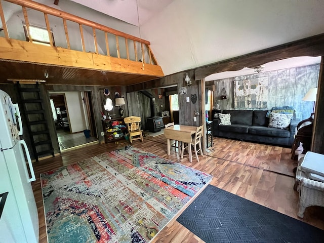 living room featuring wooden walls, a wood stove, a towering ceiling, and wood finished floors