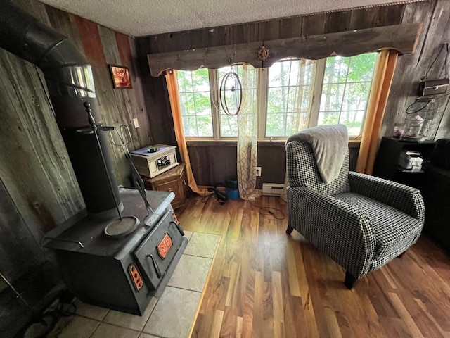 living area featuring a baseboard heating unit, wood walls, a wood stove, wood finished floors, and a textured ceiling