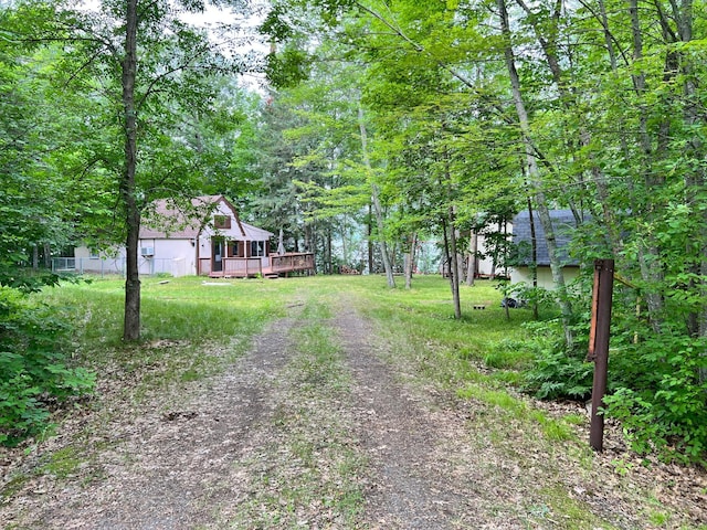 view of yard featuring a forest view, a deck, and dirt driveway