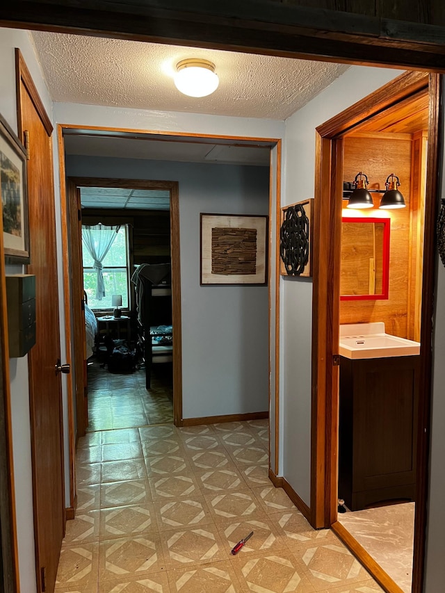 hall with a textured ceiling, light floors, and baseboards