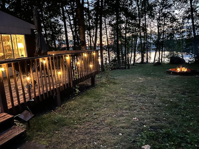 view of green lawn featuring an outdoor fire pit and a wooden deck