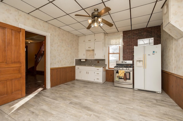 kitchen with white refrigerator with ice dispenser, stainless steel range with gas stovetop, light wood-style flooring, and wainscoting