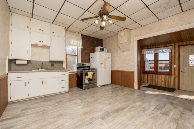 kitchen with a wainscoted wall, light wood-style flooring, white cabinets, a sink, and white appliances