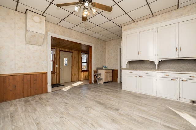 kitchen featuring a wainscoted wall, white cabinetry, light wood-style flooring, and wallpapered walls