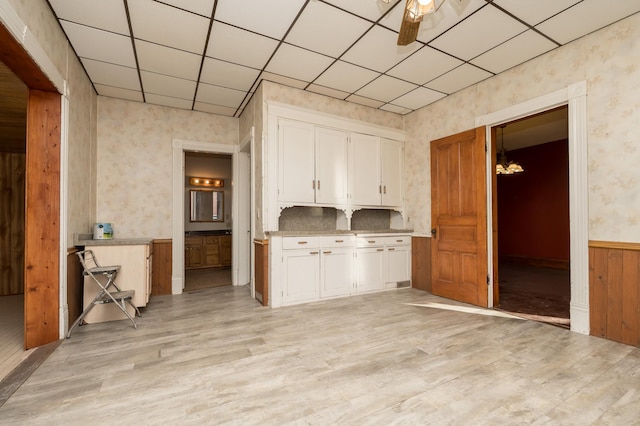 kitchen with a drop ceiling, white cabinetry, light wood-style floors, wainscoting, and wallpapered walls