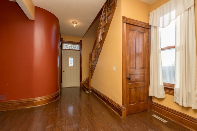 interior space with stairway, baseboards, visible vents, and dark wood-style flooring