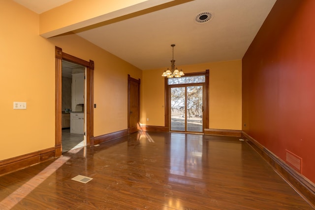 spare room with baseboards, wood finished floors, visible vents, and an inviting chandelier