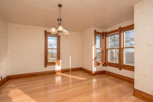 spare room featuring baseboards, an inviting chandelier, wood finished floors, and wallpapered walls