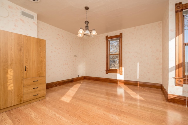 spare room with wallpapered walls, visible vents, baseboards, light wood-style flooring, and a chandelier