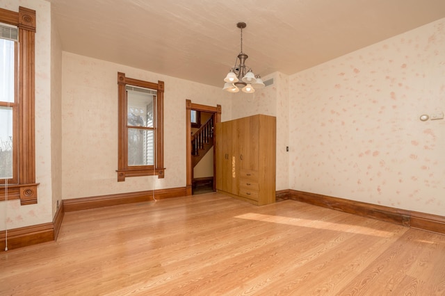 unfurnished dining area with wallpapered walls, baseboards, light wood-style flooring, stairway, and a notable chandelier