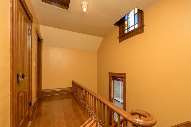 corridor featuring vaulted ceiling, a textured ceiling, an upstairs landing, baseboards, and hardwood / wood-style flooring