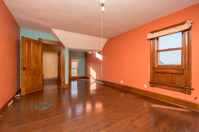 unfurnished room with a textured ceiling, wood finished floors, lofted ceiling, and baseboards