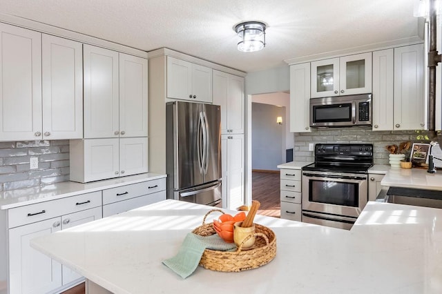 kitchen featuring stainless steel appliances, tasteful backsplash, light countertops, and glass insert cabinets