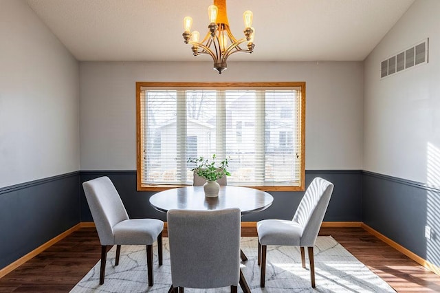 dining room with lofted ceiling, a notable chandelier, wood finished floors, visible vents, and baseboards