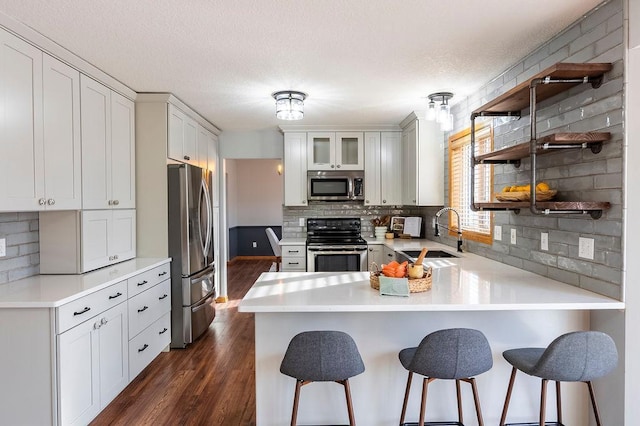 kitchen with dark wood-style floors, open shelves, appliances with stainless steel finishes, a sink, and a peninsula