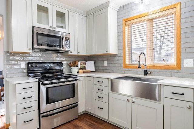 kitchen featuring stainless steel appliances, a sink, light countertops, backsplash, and dark wood-style floors