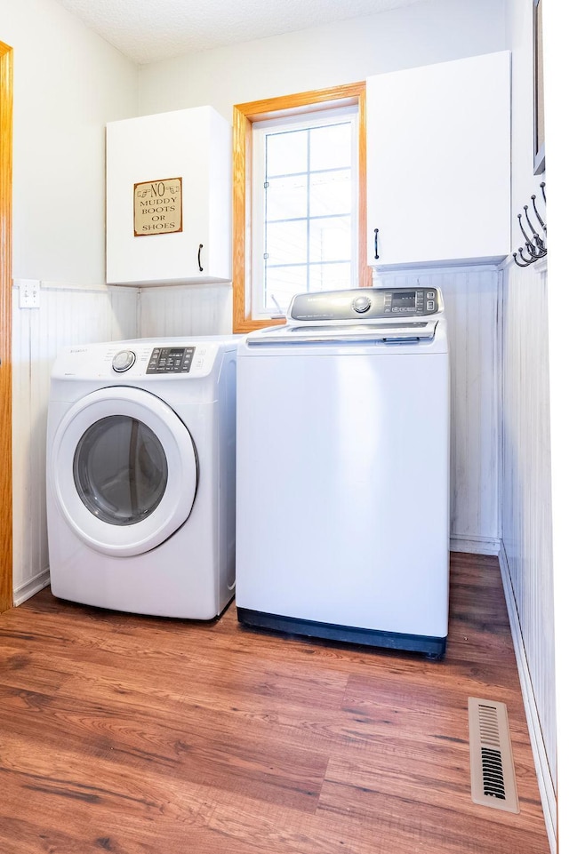 clothes washing area with cabinet space, washing machine and dryer, visible vents, and light wood-style floors