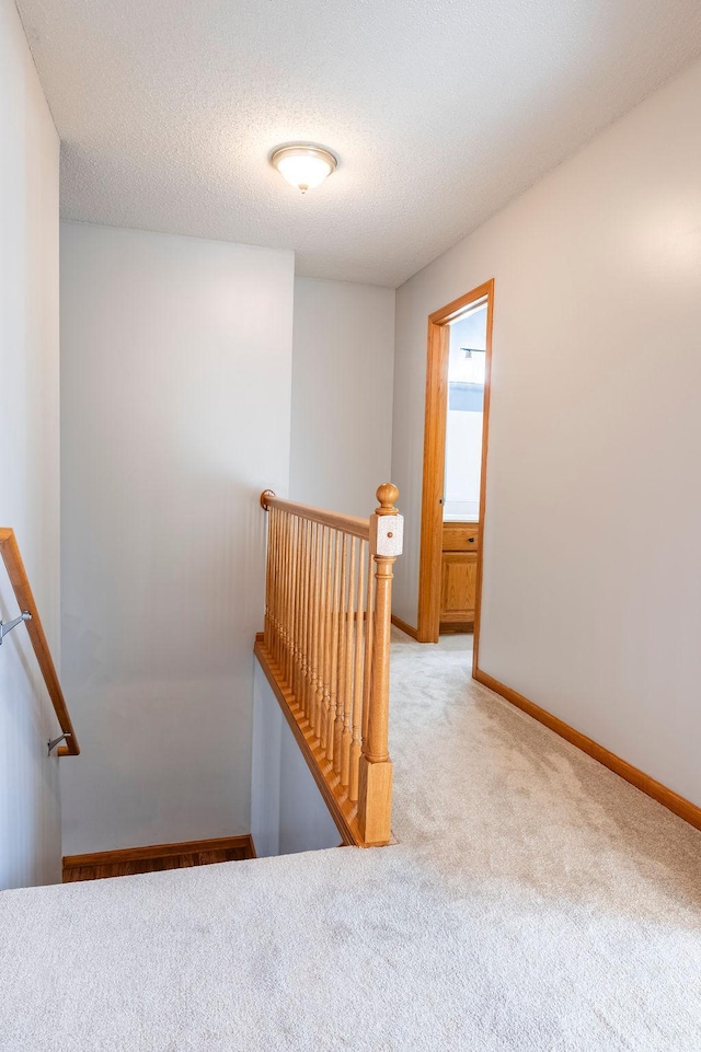 staircase with carpet flooring, a textured ceiling, and baseboards