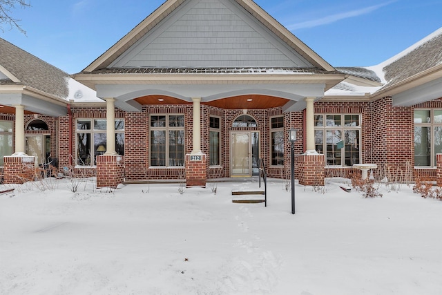 snow covered back of property featuring covered porch and brick siding