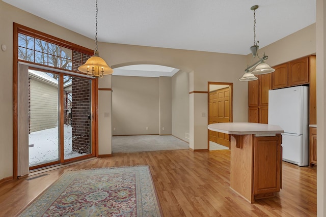 kitchen with arched walkways, a kitchen island, light countertops, light wood-type flooring, and freestanding refrigerator